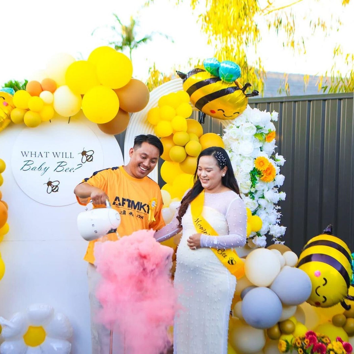 Gender reveal smoke bombs creating pink smoke at bee-themed party with yellow balloon arch and decorative backdrop