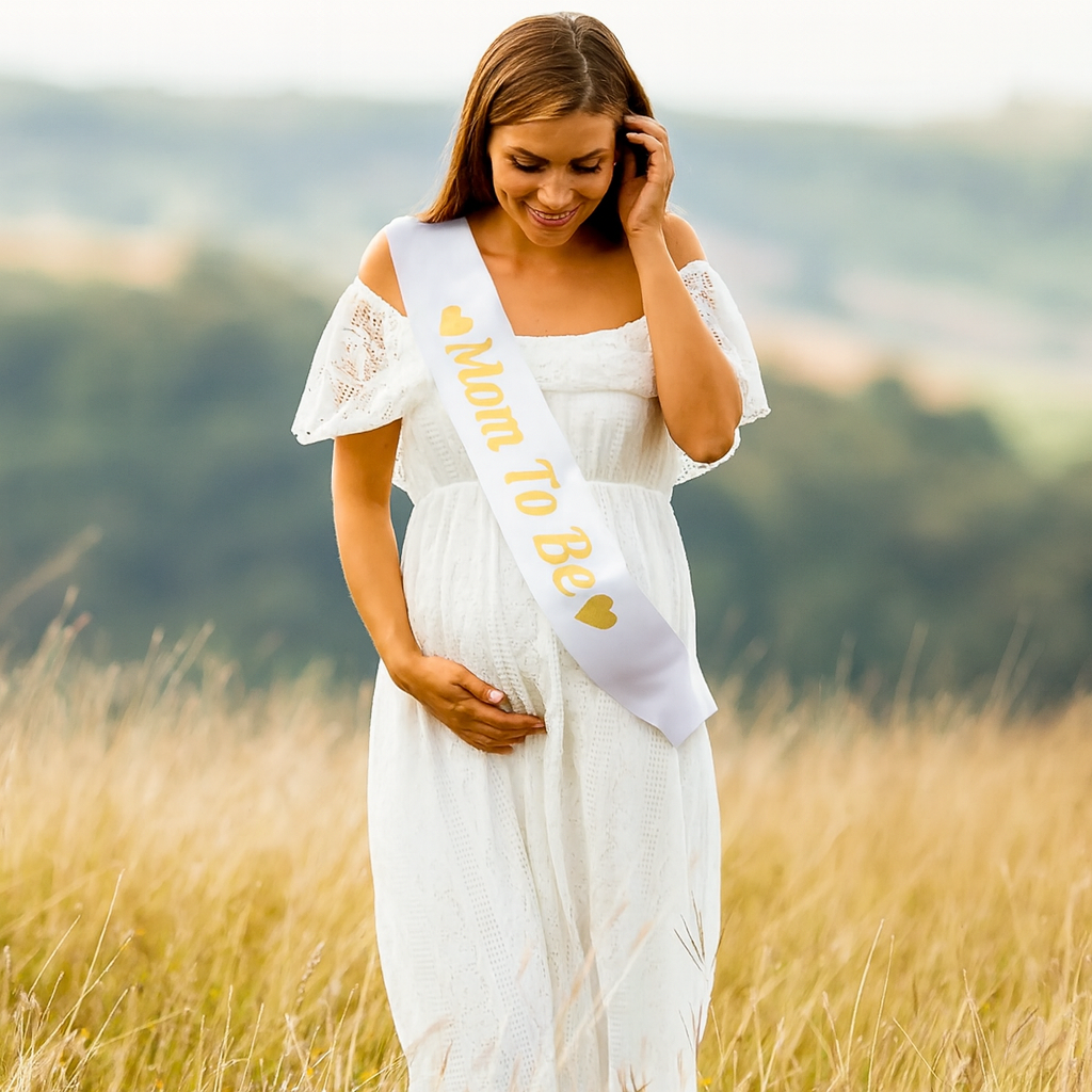 Satin "Mom To Be" Gender Reveal Sash worn by pregnant woman in white dress outdoors in field.