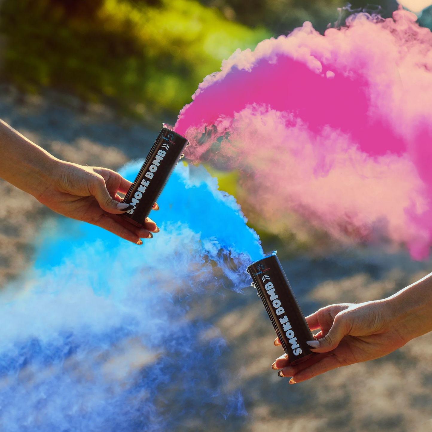 Gender reveal smoke bombs releasing vibrant blue and pink smoke clouds in outdoor sunlit setting