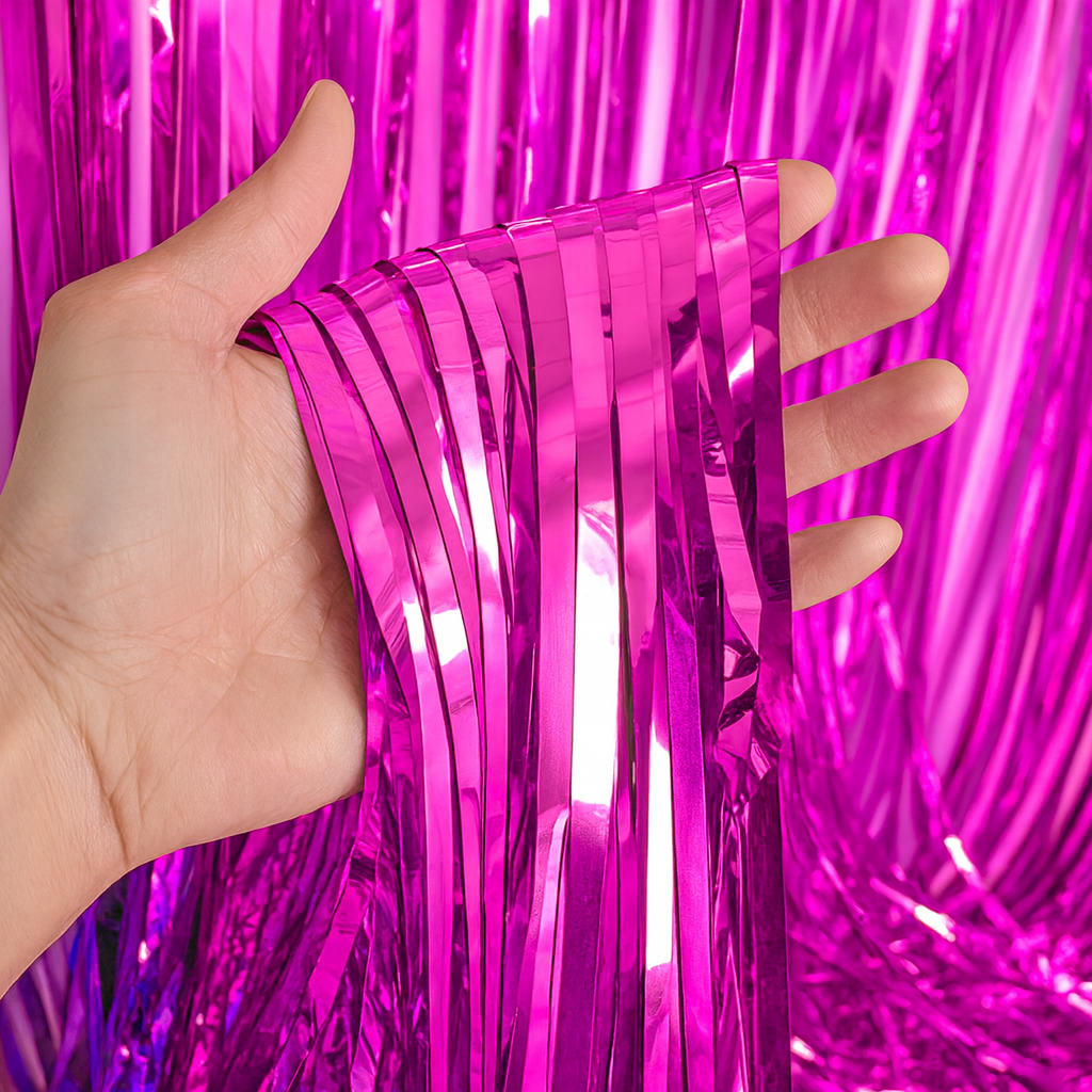 Hand holding shiny metallic pink strands of the Gender Reveal Foil Party Curtain backdrop for celebrations.